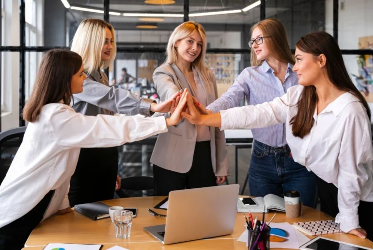 A group of business women joining their hands together in the office.
