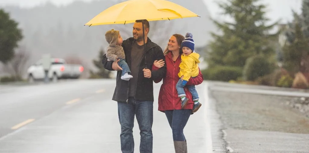 A family holding their children and an umbrella in the rain