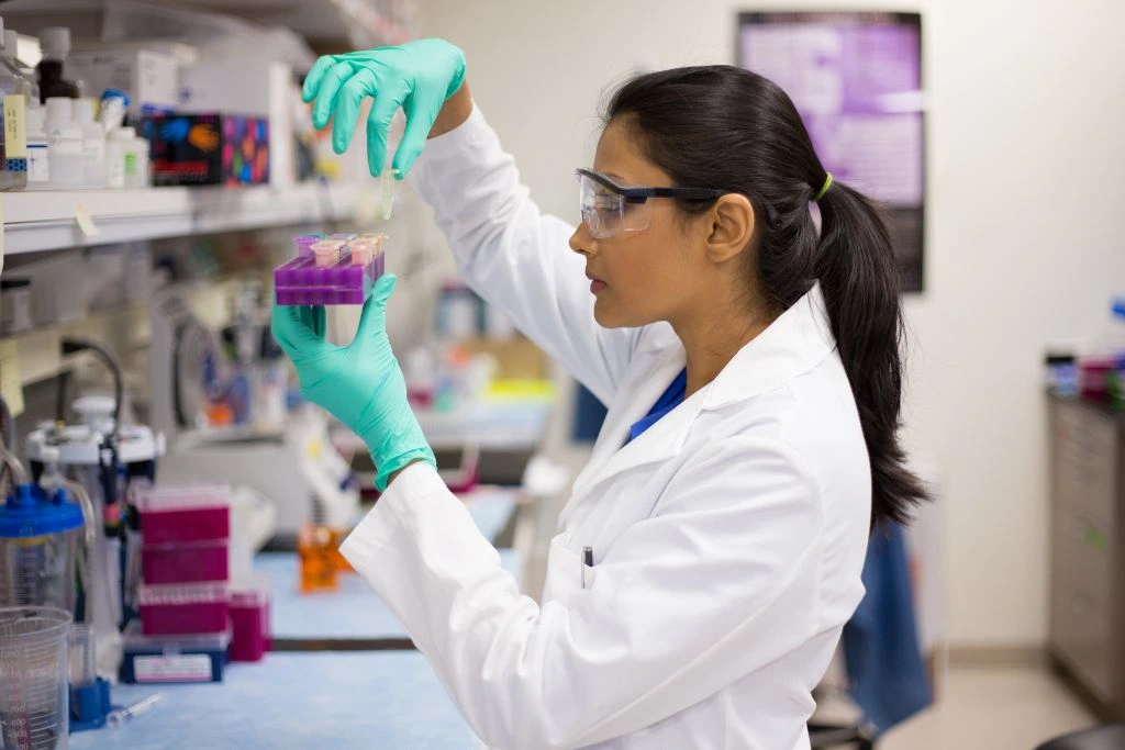A woman in a lab coat holding a set of samples and looking at it.
