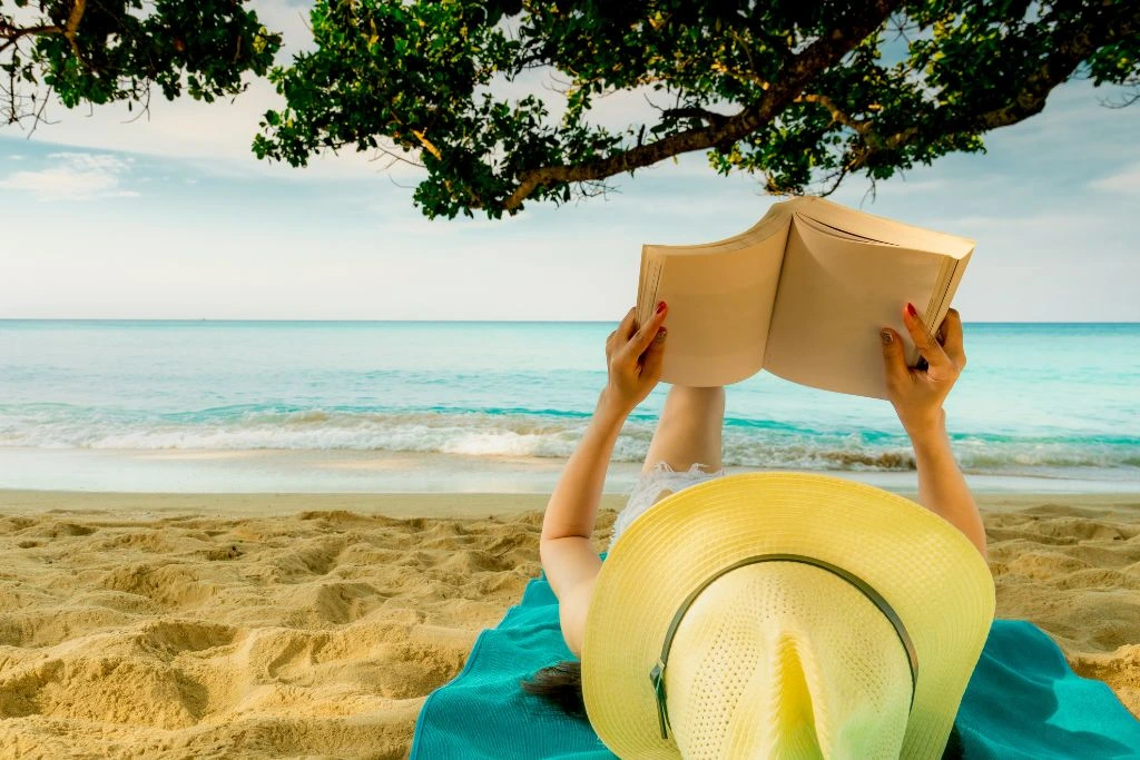 A person reading a book while lying down on a towel at the beach