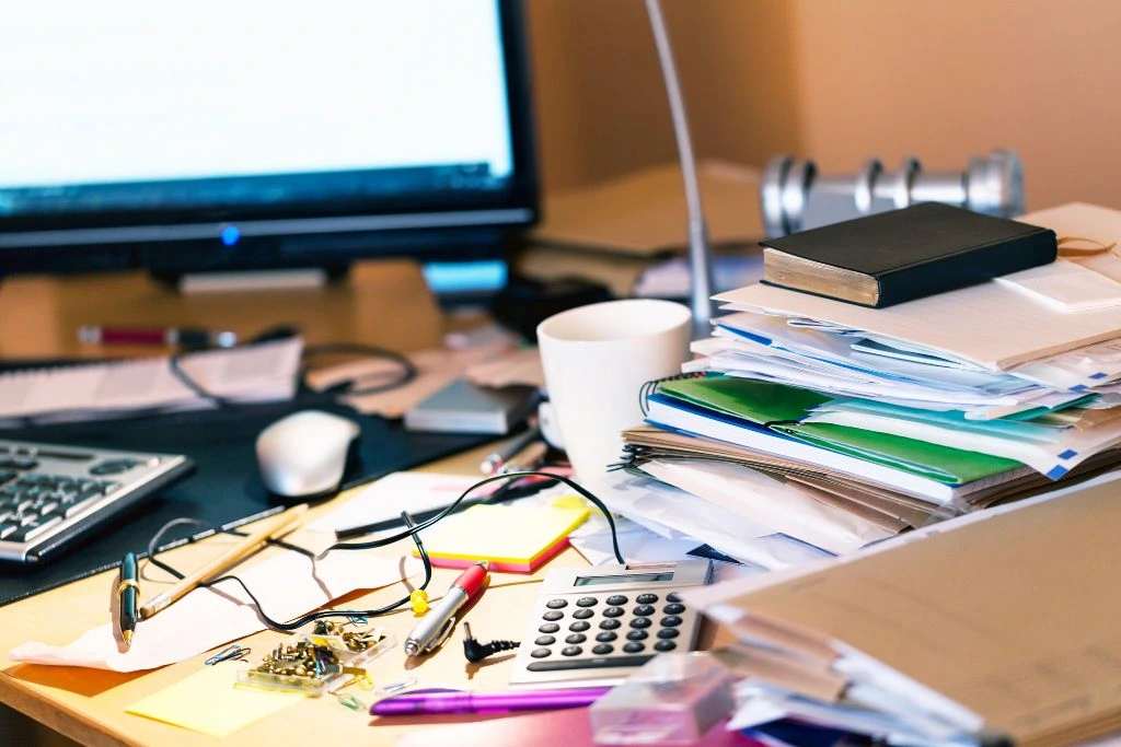 a messy desk cluttered with paper, calculator and other stuff