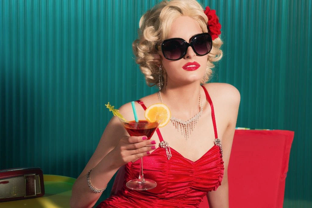A woman dressed as Marylin Monroe in her red signature swimsuit, wearing her sunglasses and holding a cocktail