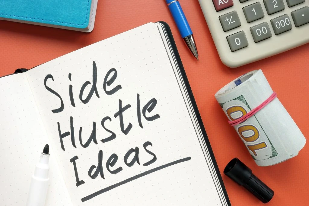 A note has a "side hustle" written on it beside a roll of cash, calculator, and pen