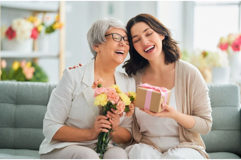 mother and daughter sitting on a coach holding flowers and gifts