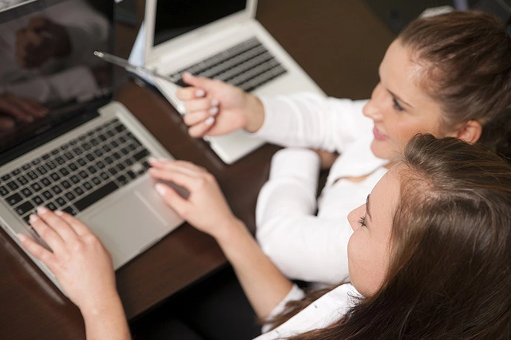 A woman coaching her co-worker in front of the laptop