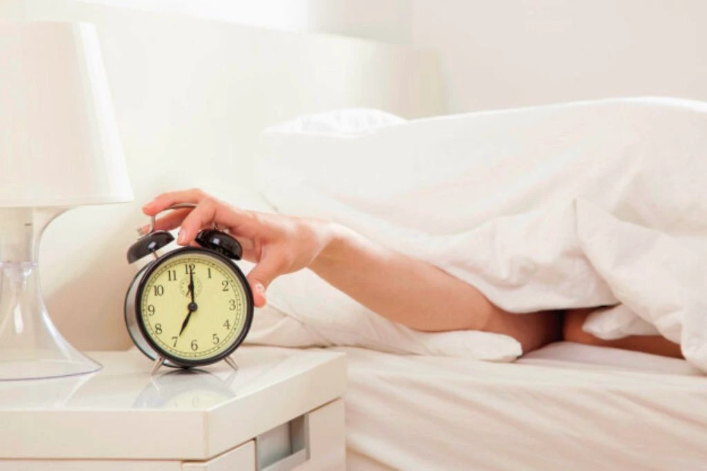 A gentle ringing from the alarm clock on a bedside table rouses a sleeping person to start their day