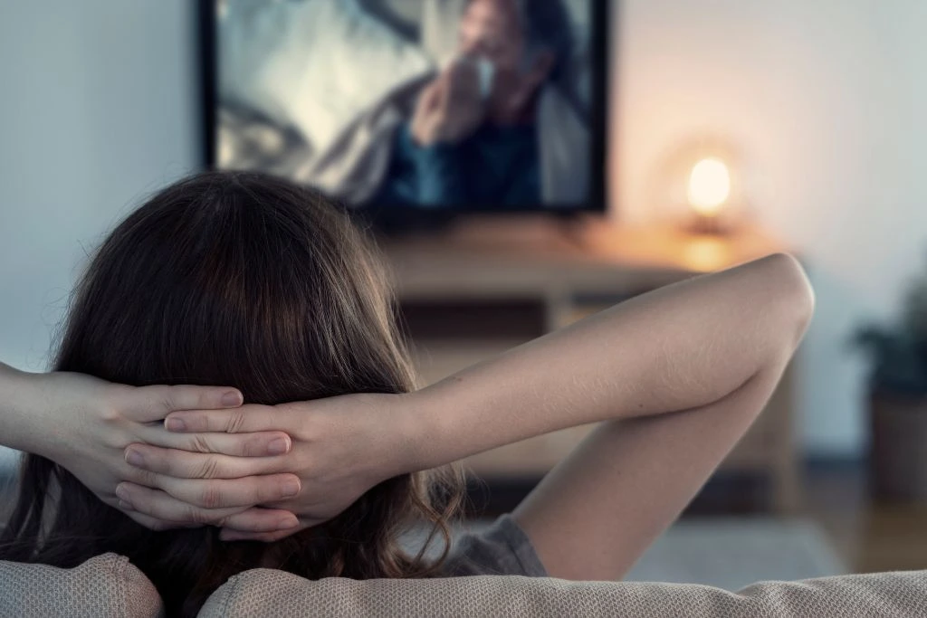 woman sitting on her couch in hands behind her neck while watching tv