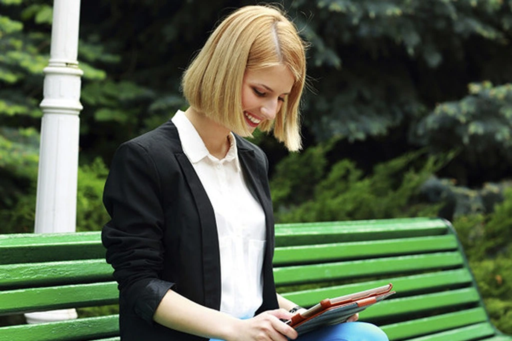 A woman sitting on a bench while looking at her tablet