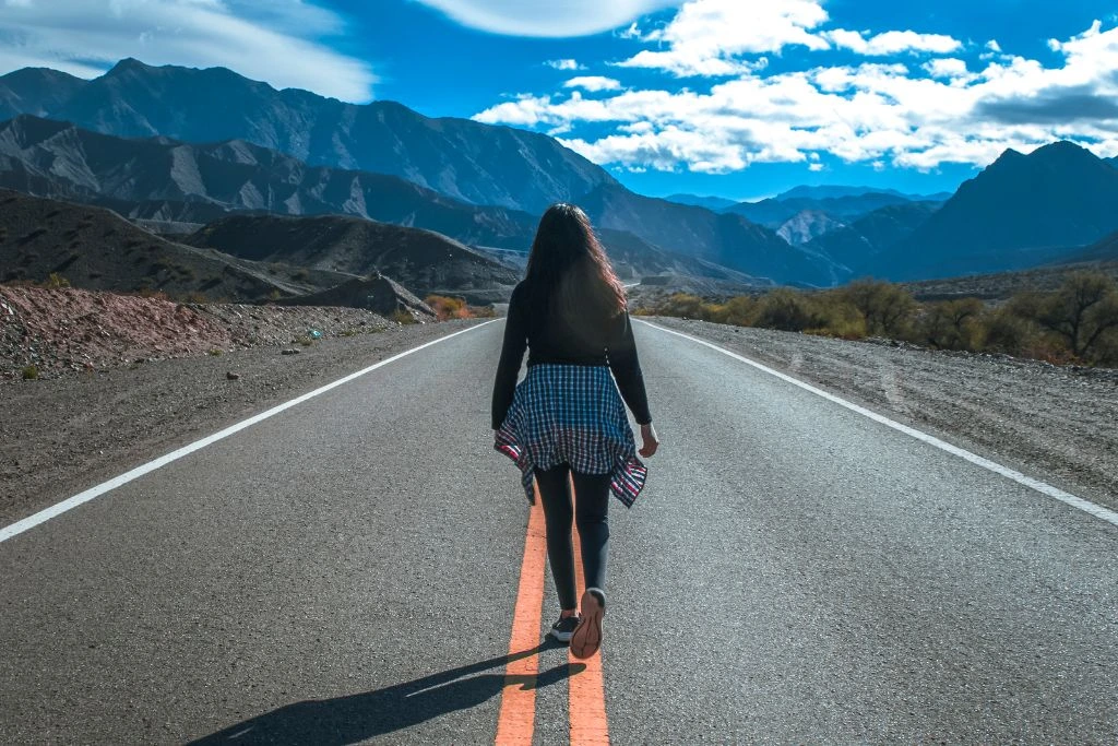 A back view of a woman walking on a road facing the mountains