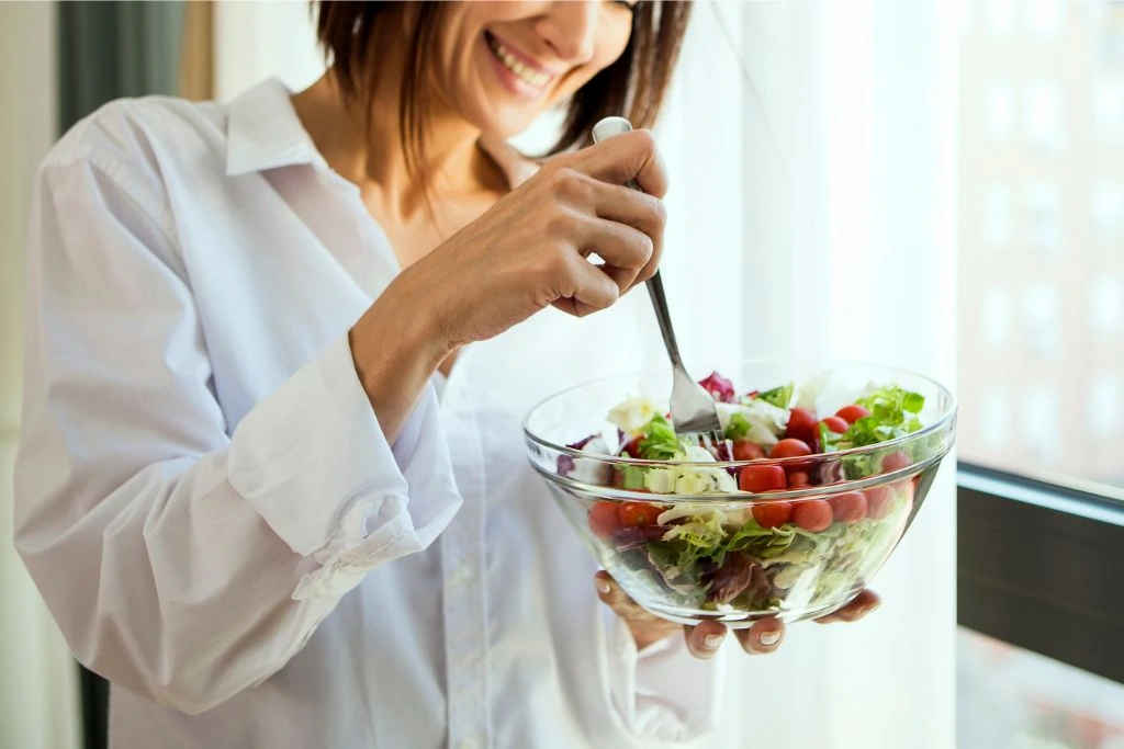 woman eating a bowl of salad by the window