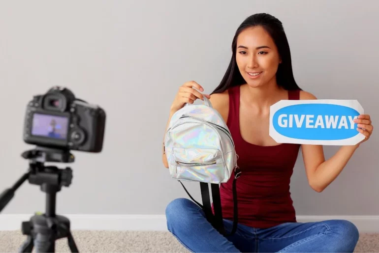 woman in front of a camera holding a giveaway sign