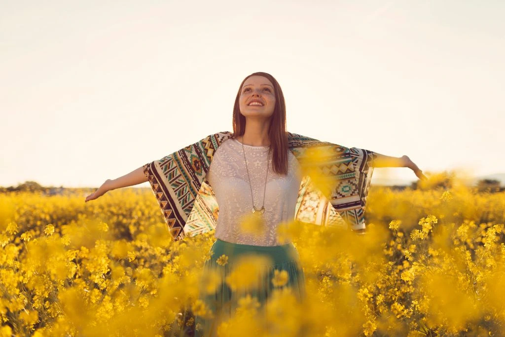 A woman in the middle of a blooming hyacinth field as she looks up happily with arms wide open.
