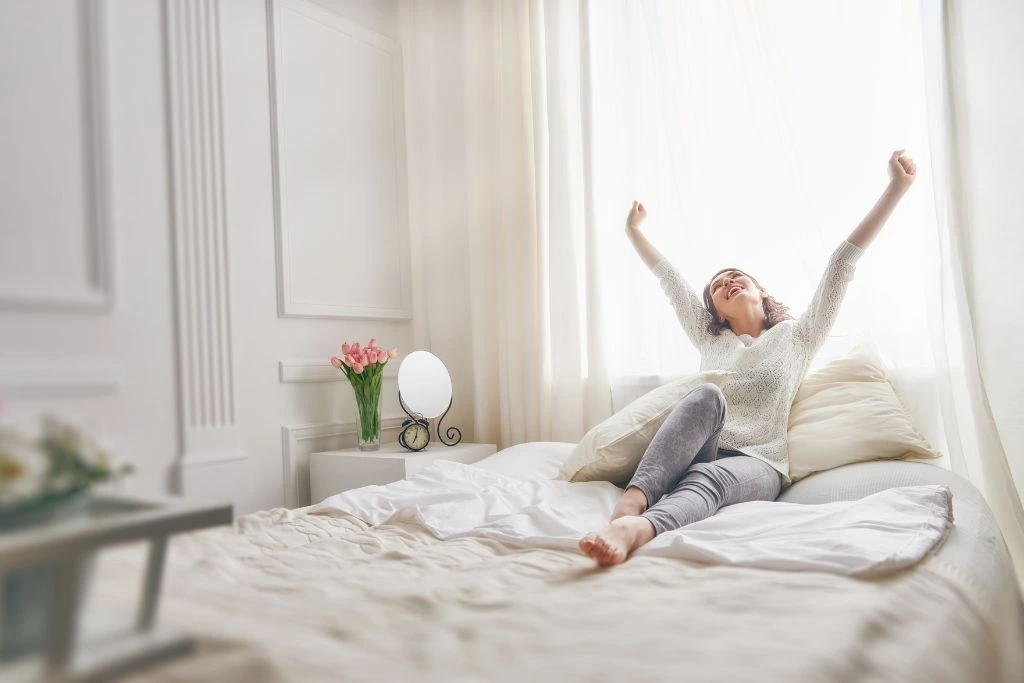 A woman stretching her arms upwards while sitting at her bed