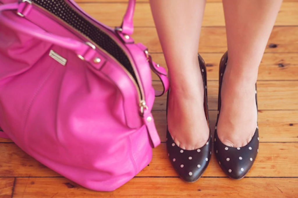 woman standing with stilettos beside a pink bag
