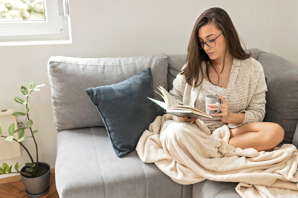 A woman is enjoying her book and cup of coffee while relaxing on a comfortable sofa.