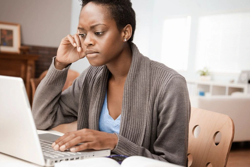 An African American woman sitting in front of her laptop looks worried about something.