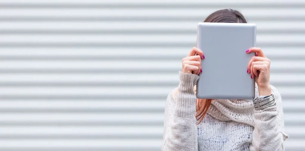 A woman standing while covering her face with a tablet