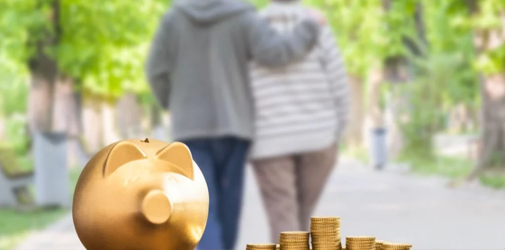 2 old people walking behind a table with coins and piggy bank