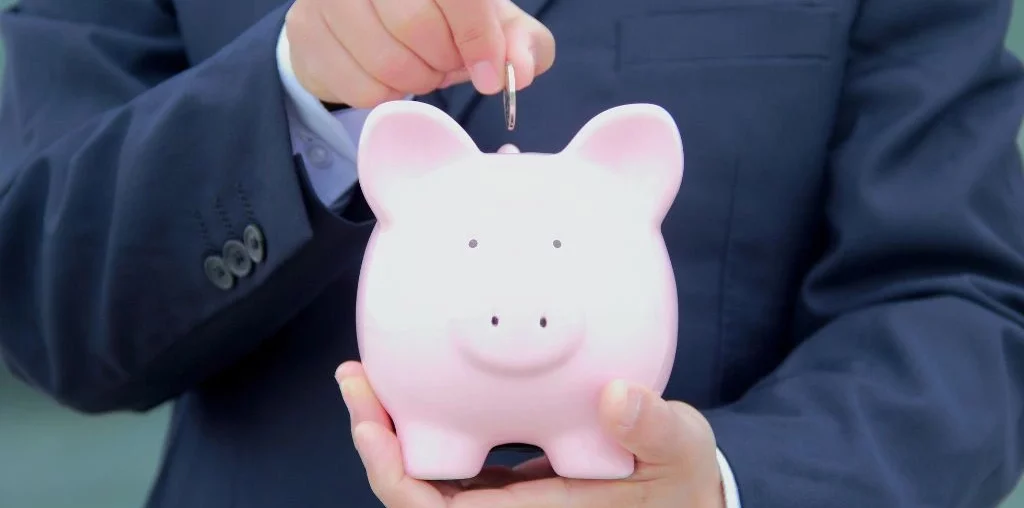 A person inserting a coin to the piggy bank