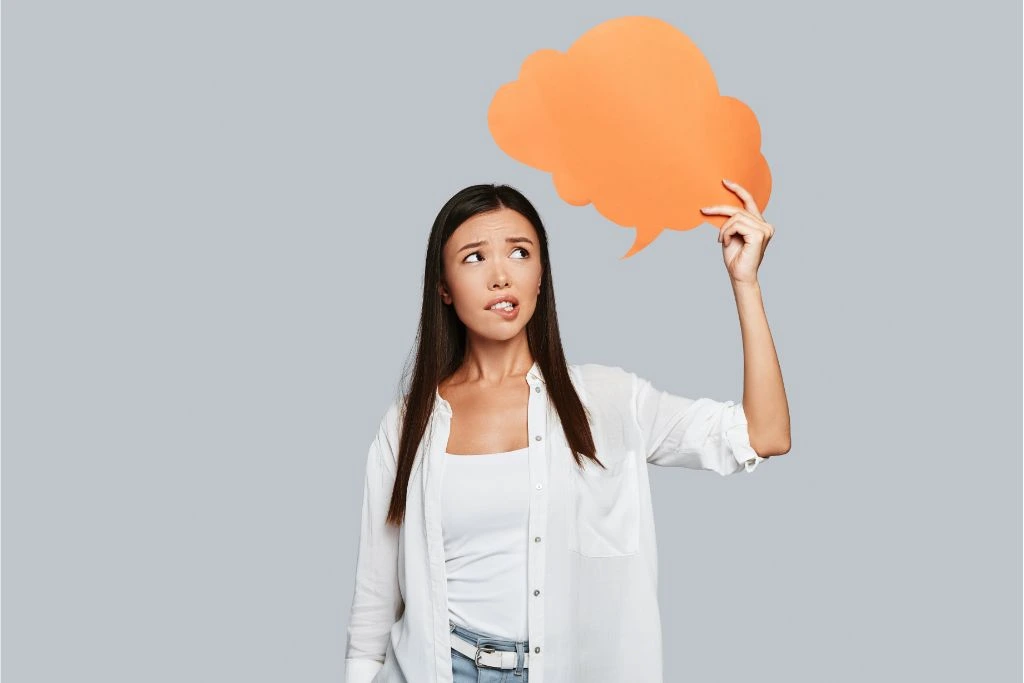 woman holding an orange paper thought bubble on gray background