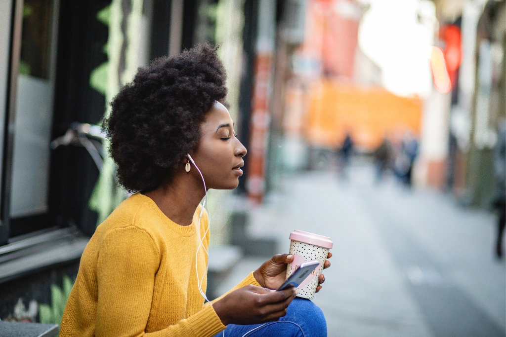woman on the street listening to her phone while having a coffee