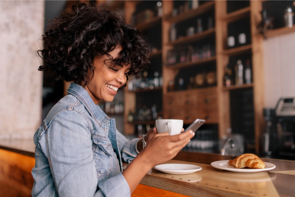 woman looking at her phone while holding a cup on the other hand