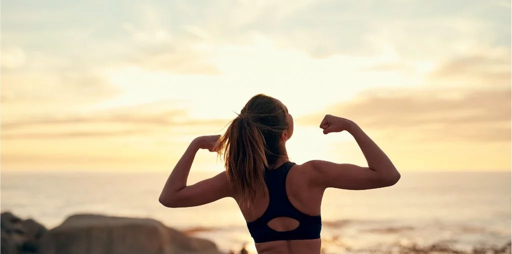 woman in running outfit flexing her arms at sunrise