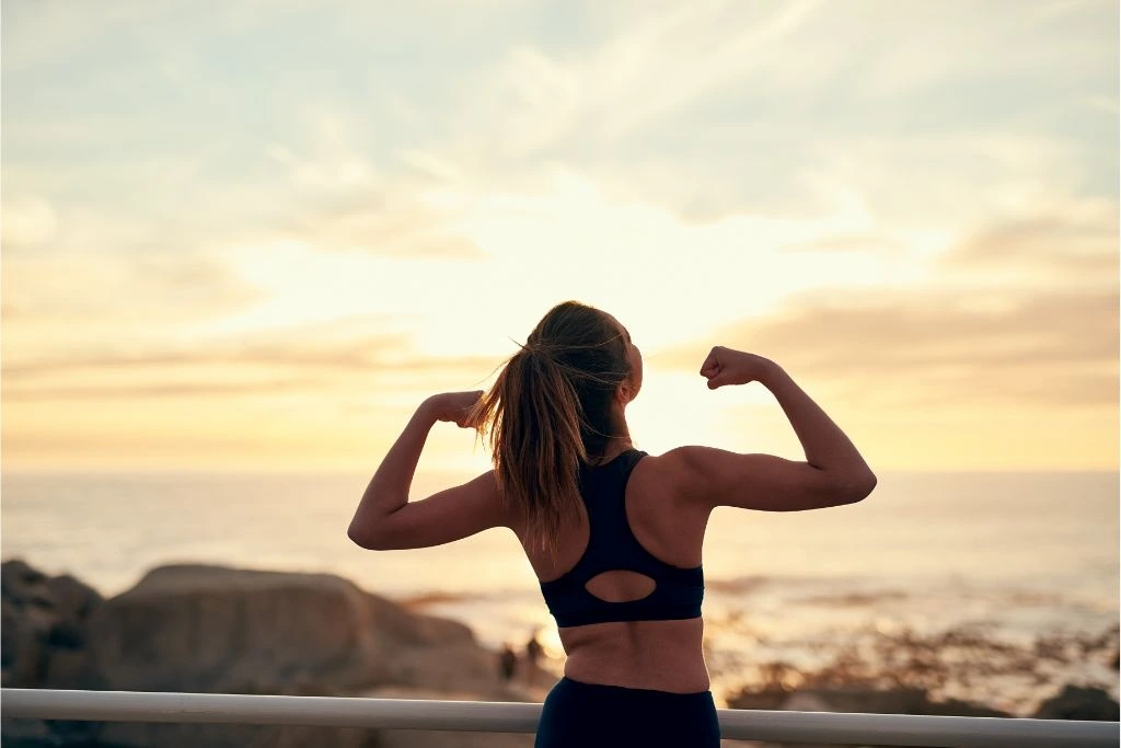 woman in running outfit flexing her arms at sunrise