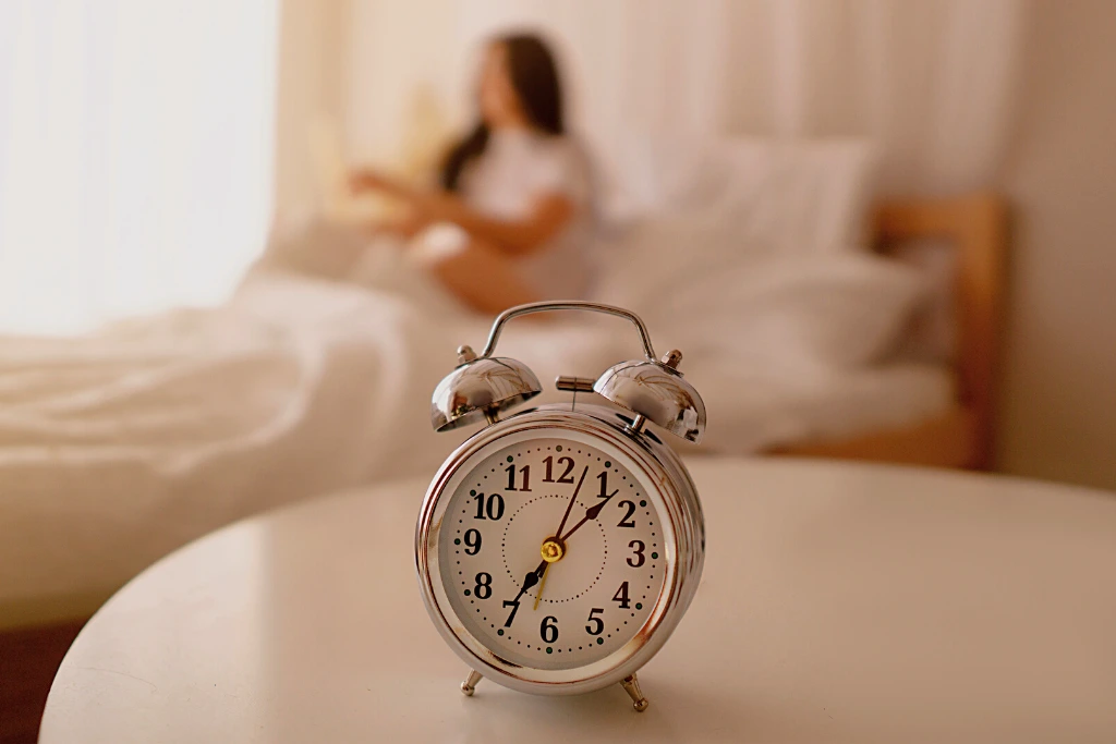 On top of a small table, an alarm clock creates a backdrop for the woman who just woke up