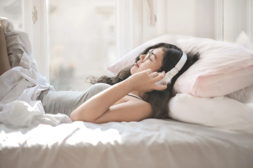 A young woman lying on her bed and enjoying music through her headphones.