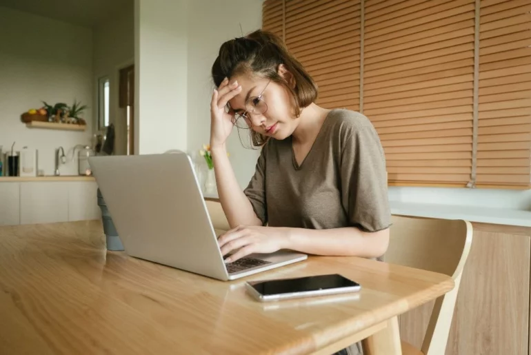 A woman holding her head while in front of her laptop