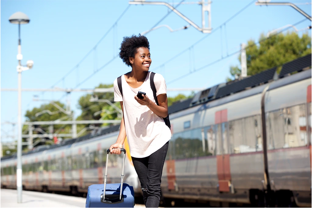 woman holding bag and phone with a train behind her