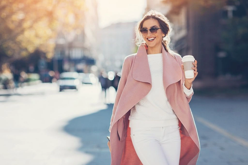 woman walking down the street holding a cup of coffee