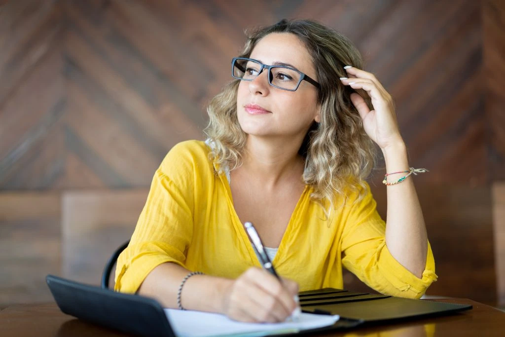 woman sitting at her desk writing down ideas on her notebook