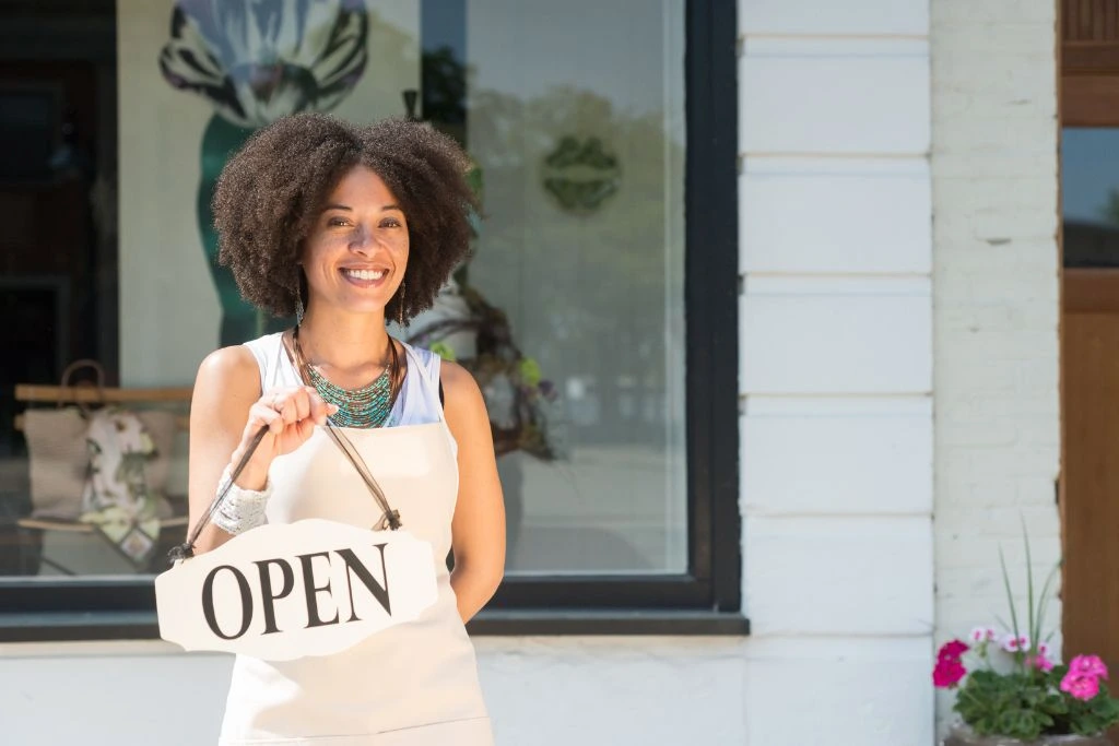 female business owner holding up an open sign in front of her store