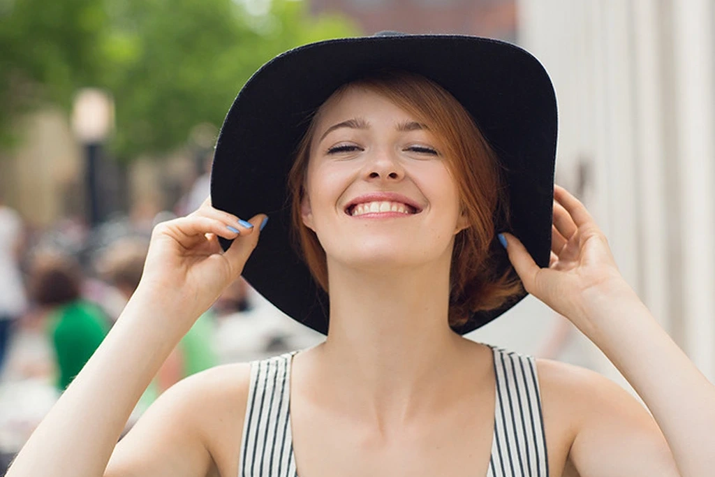 a woman smiling while holding her hat
