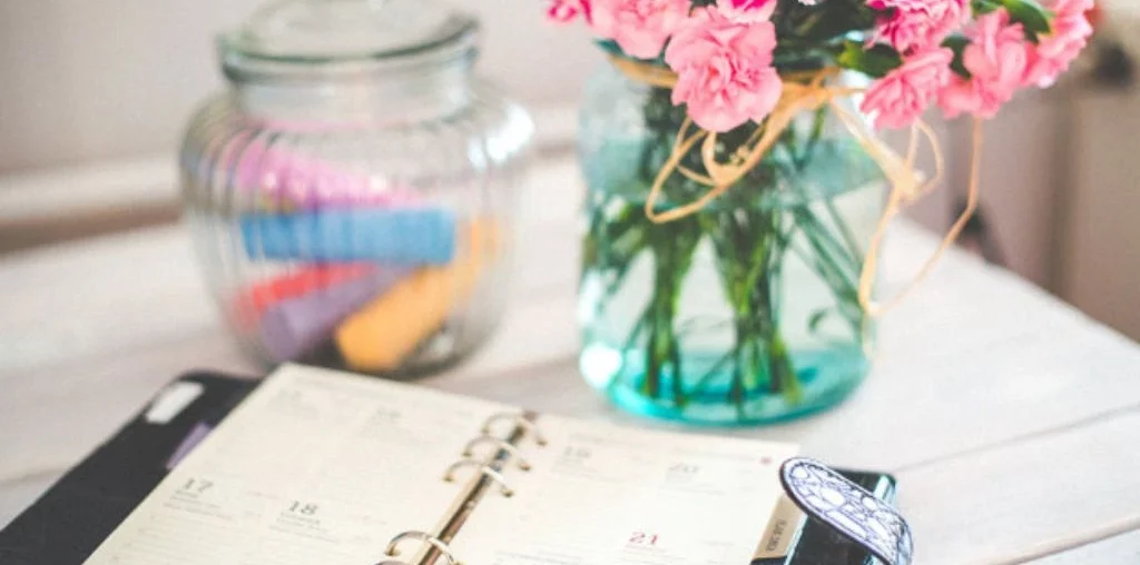 Planner, pink flower and jar of rolled paper on the table