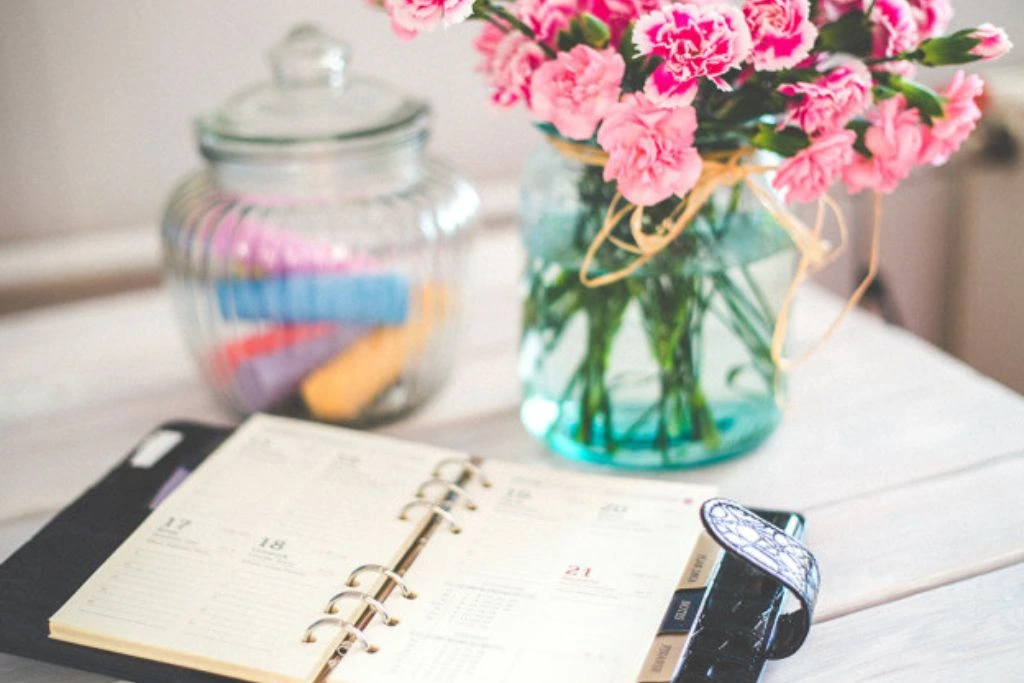 Planner, pink flower and jar of rolled paper on the table