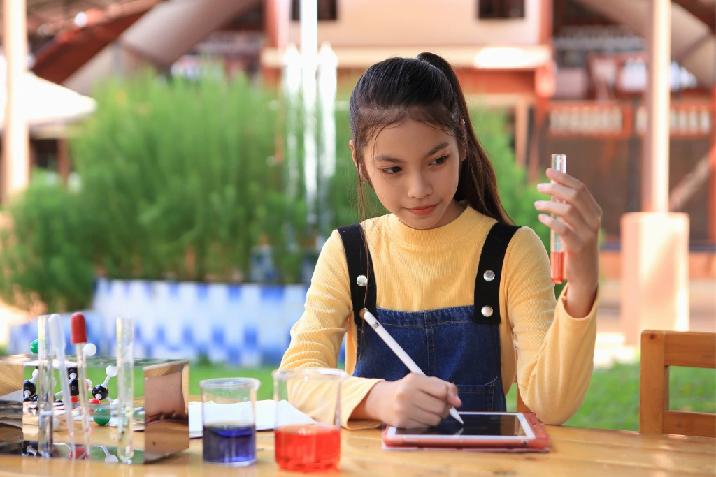 a young girl holding up a test tube while writing some notes on her tablet