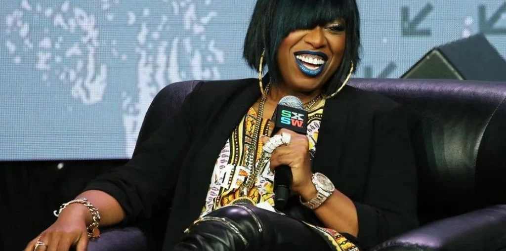 Black woman laughing while sitting on a sofa in a talk show
