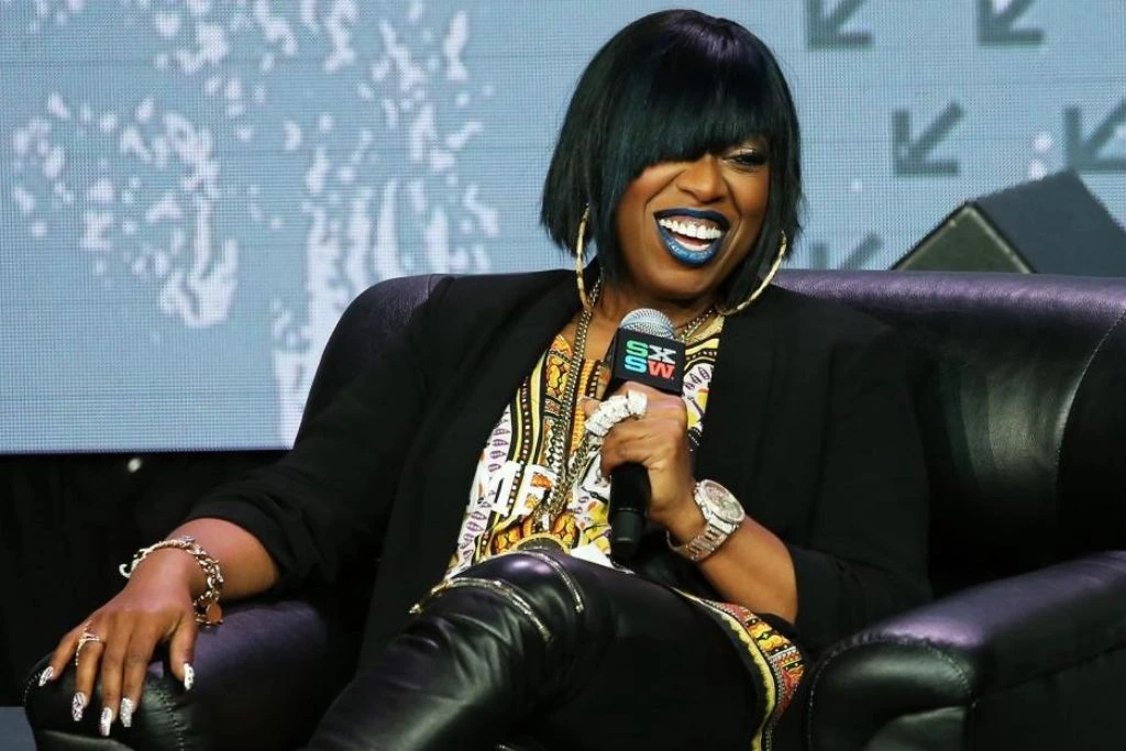 Black woman laughing while sitting on a sofa in a talk show