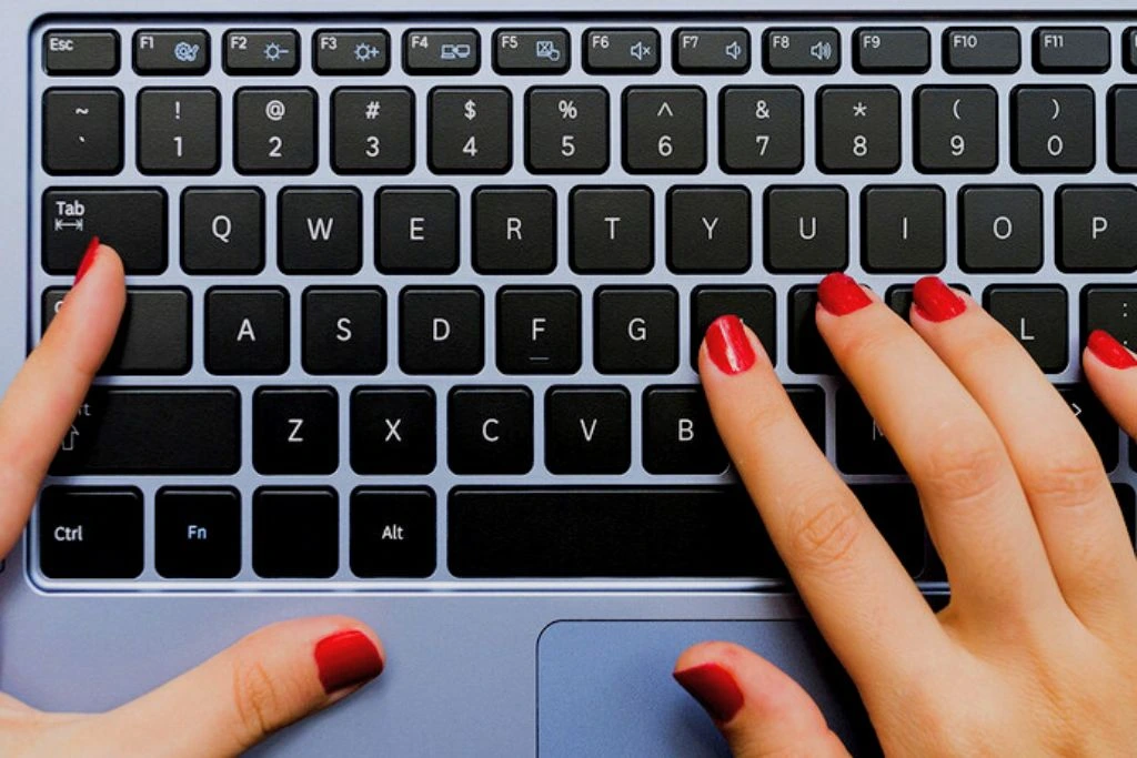 woman with red nail polish typing on her laptop