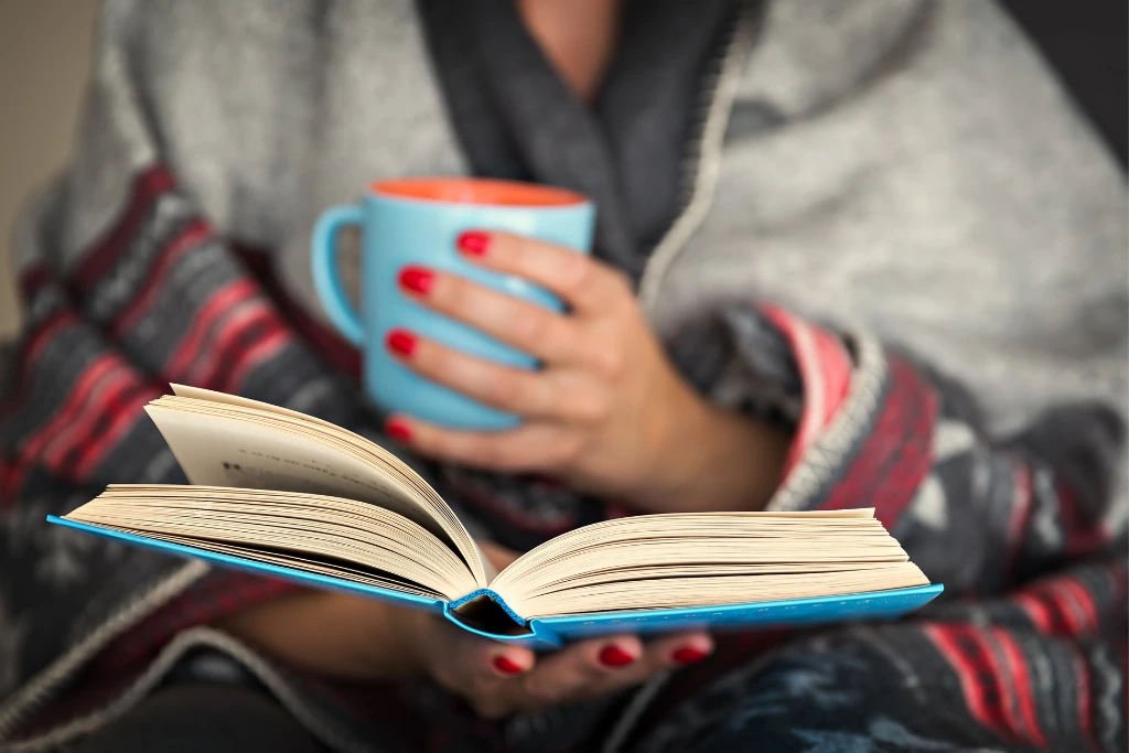 a woman reading a book while having holding a cup of drink